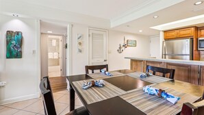 A dining area with a dark wooden table, four chairs, and a kitchen with wooden cabinets and a stainless steel refrigerator. - Coquina Condos: Ocean View, Ground Floor (St. Augustine)