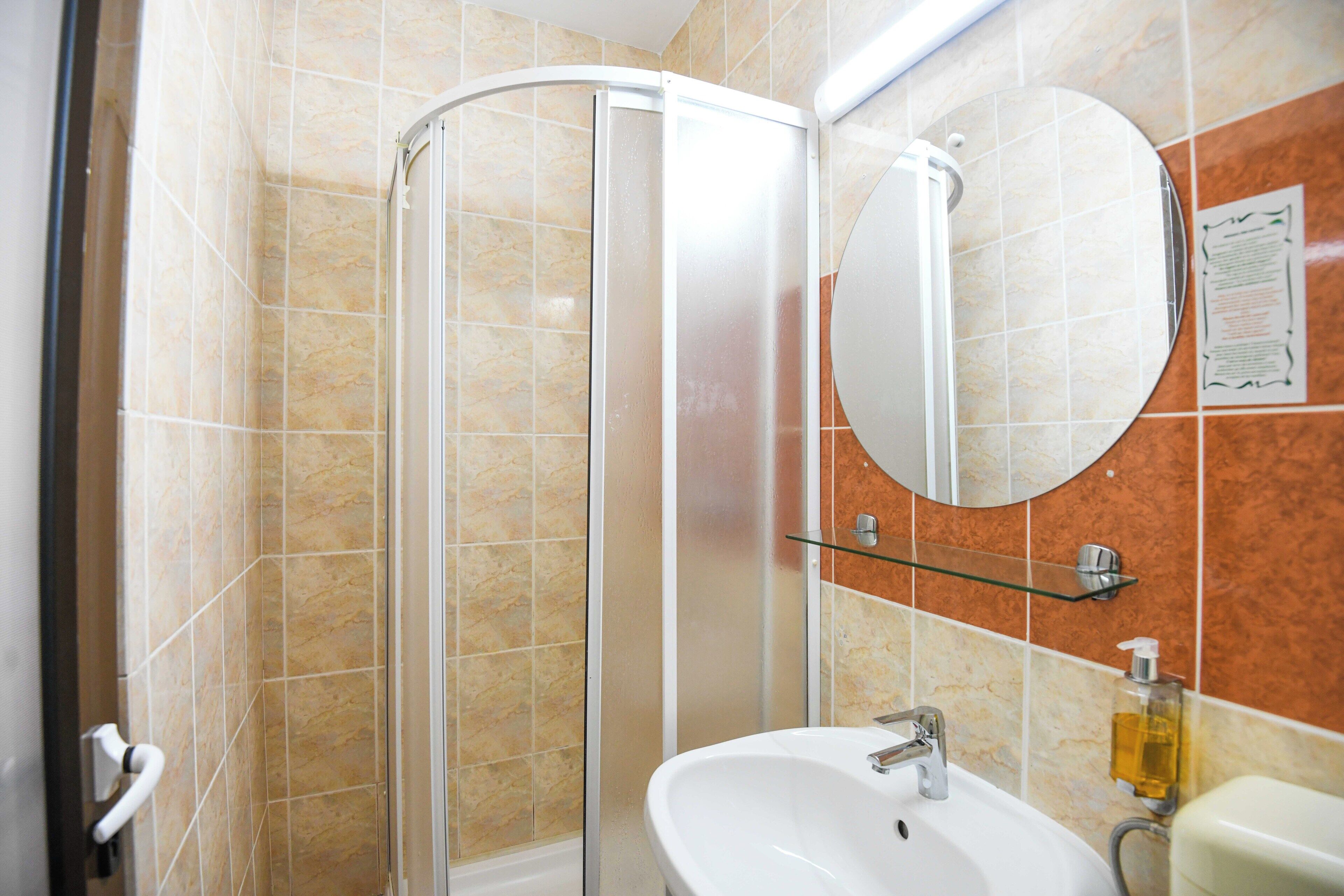 Un baño con cabina de ducha de vidrio, lavabo, espejo y dispensador de jabón.