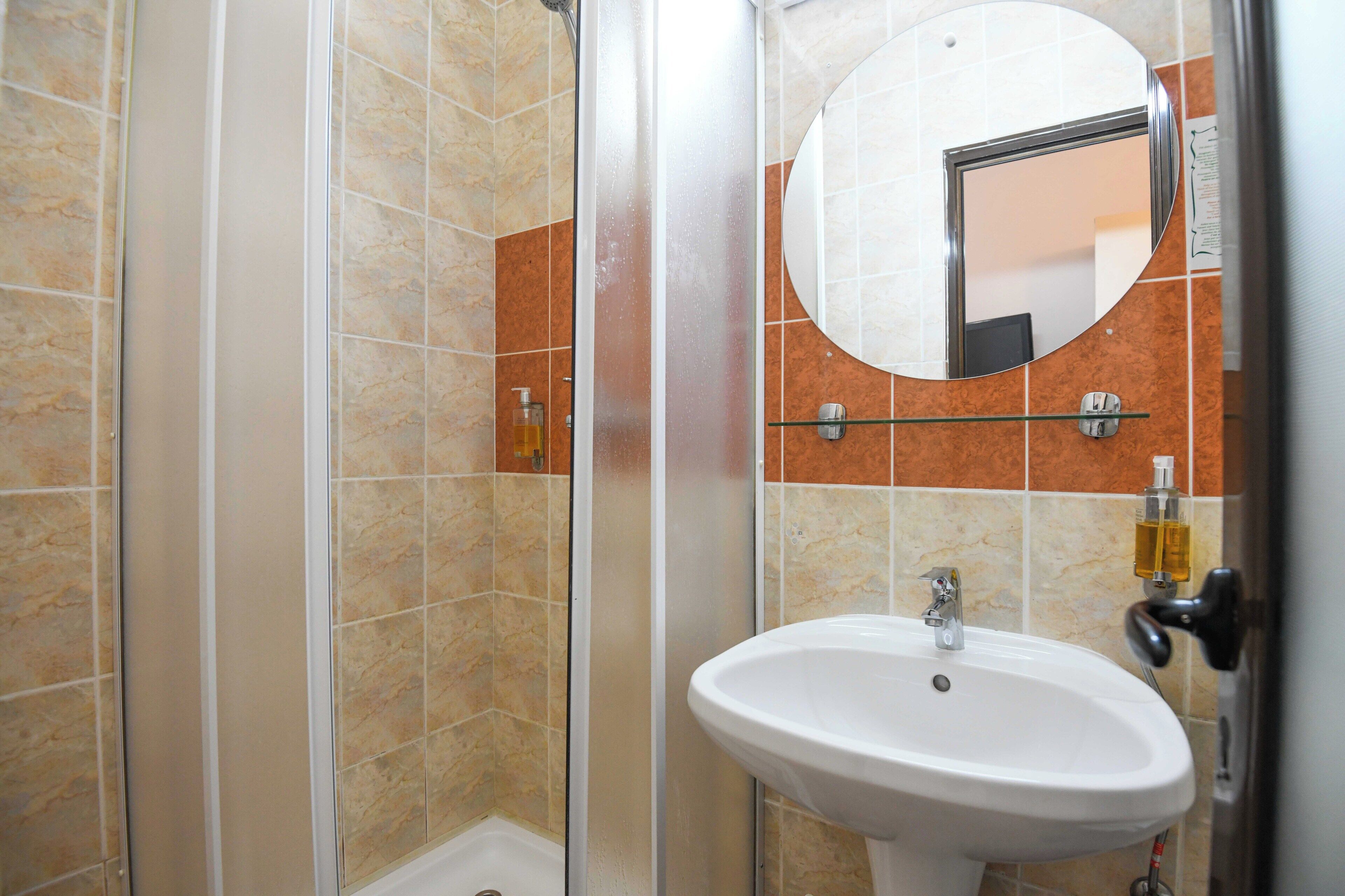 A bathroom with a shower enclosure, a sink, and a mirror.