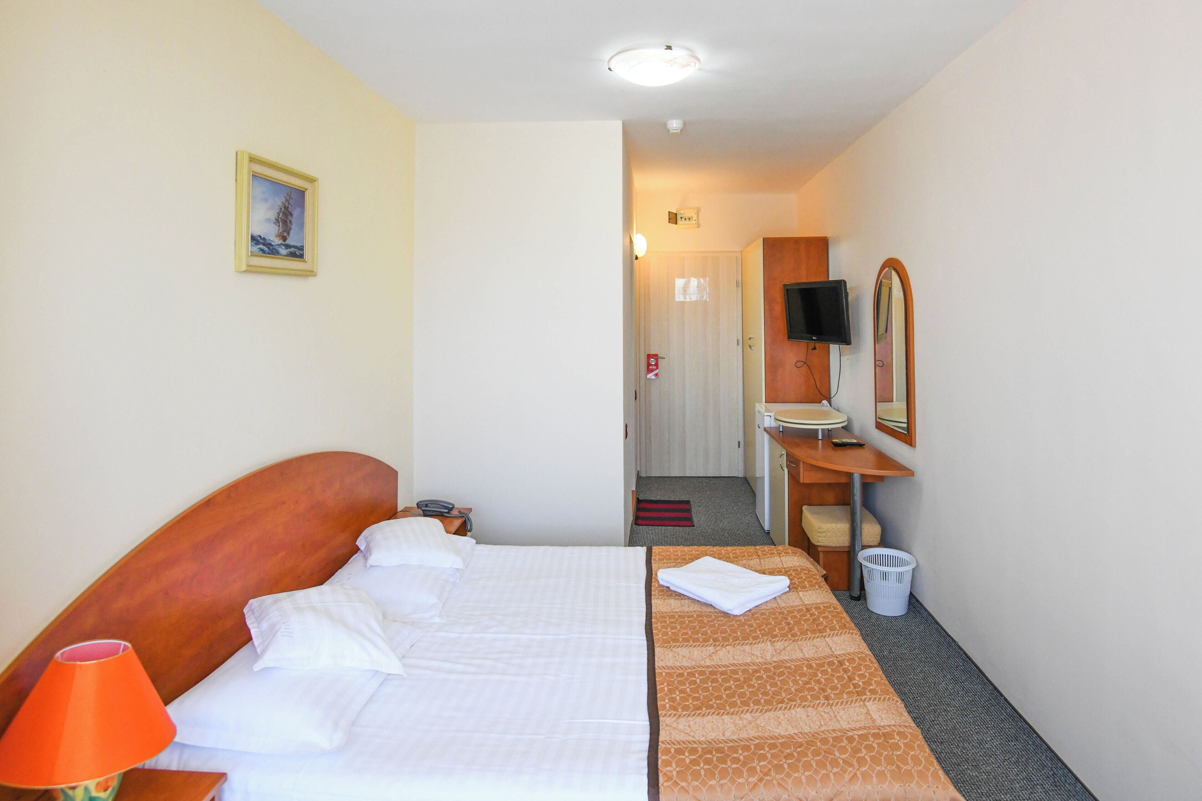 A hotel room with a bed, a desk, a chair, a television, and a mirror.