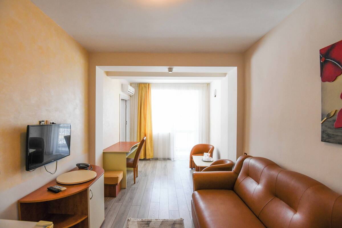 A compact hotel room with a sofa, a small dining table, a TV, and a desk.