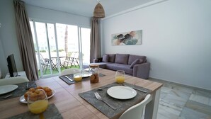 A dining area with a table set for breakfast, a sofa, and a large window with a view of the outdoors. - Sunstay Relax 56 Rio Marina Nerja (nerja)
