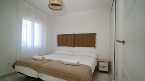 A bedroom with a double bed, two bedside tables, a small nightstand, and a woven headboard. - Sunstay Relax 56 Rio Marina Nerja (nerja)