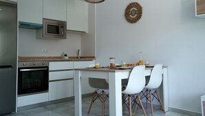 A modern kitchen with white cabinets, a built-in microwave, and a wooden countertop. There is a dining area with a table and four chairs. - Sunstay Relax 56 Rio Marina Nerja (nerja)