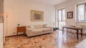 A living room with a beige sofa, a dining table with chairs, a patterned floor, and artwork on the walls. - Madamart - 301 Autodromof1 Centro (Monza)