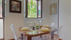 A dining room with a wooden table set for four, clear chairs, and a window with a view of trees. - Madamart - 301 Autodromof1 Centro (Monza)