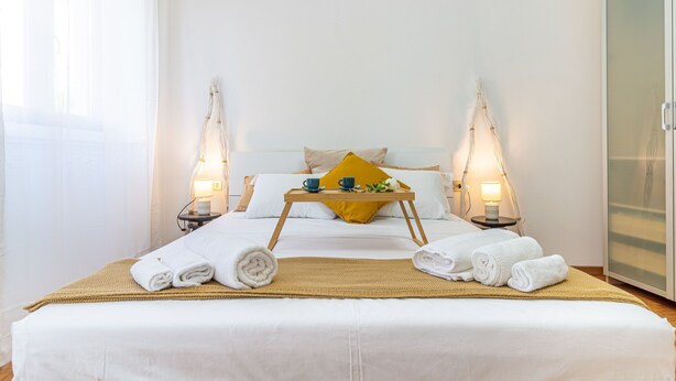 A neatly made bed with white linens, a yellow pillow, and a tray with a cup and a bowl. There are two bedside lamps and a wardrobe in the room. - Madamart - 301 Autodromof1 Centro (Monza)