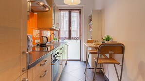 A compact kitchen with wooden cabinets, a stainless steel stove, and a dining area with a chair and table. - Madamart - 301 Autodromof1 Centro (Monza)