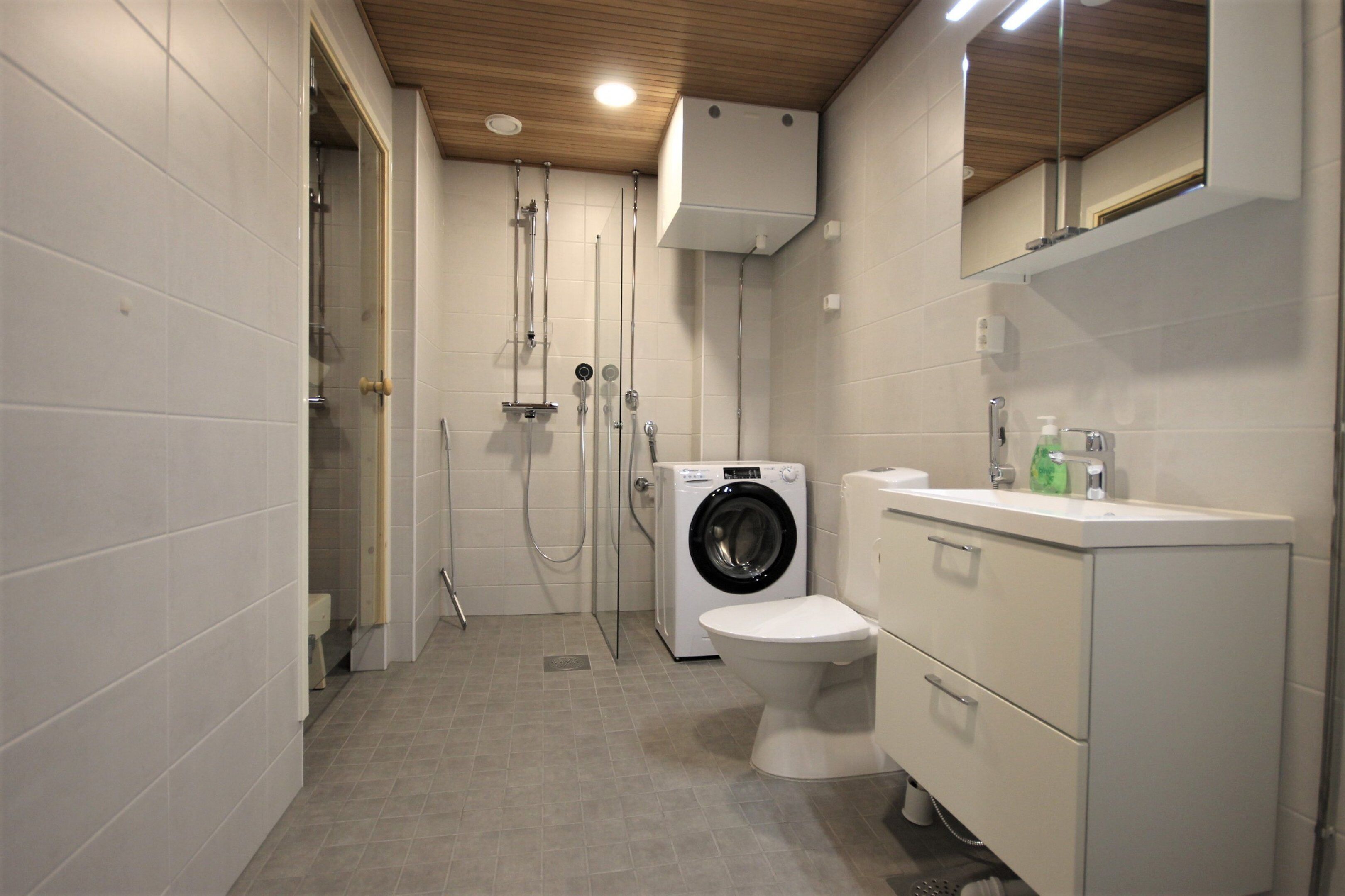 A modern bathroom with a shower, toilet, washing machine, and a sink with a mirror.