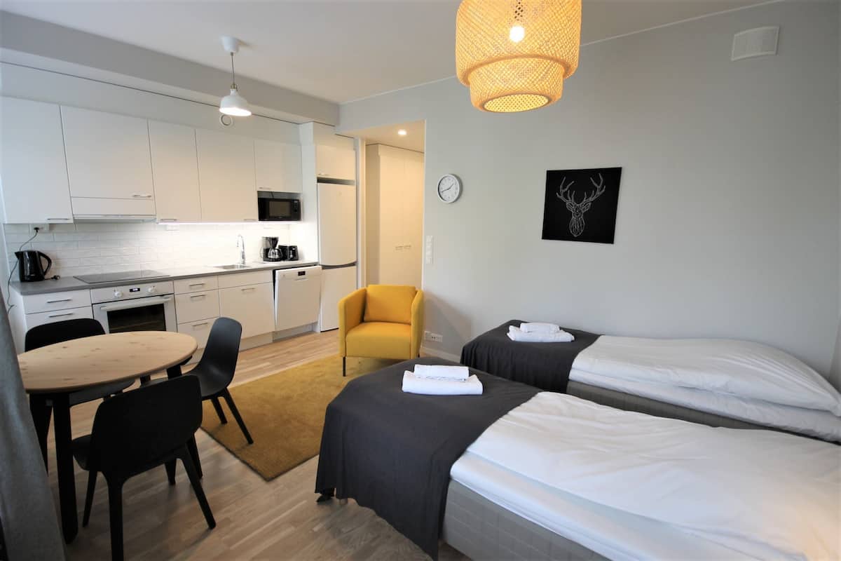 Una habitación de hotel moderna con kitchenette, dos camas, una zona de comedor y un sillón amarillo.