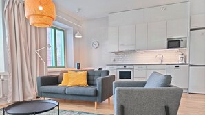 A modern apartment with a grey sofa, a small round table, and a kitchen area with white cabinets and appliances. - Forenom Serviced Apartments Kuopio (Kuopio)