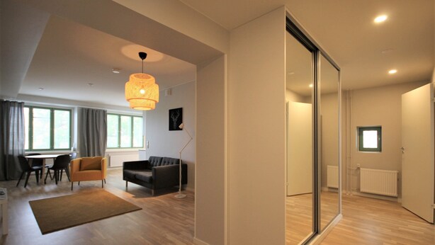 A modern living room with a sofa, armchair, and dining table. There is a large window providing natural light and a view of the outdoors. - Forenom Serviced Apartments Kuopio (Kuopio)