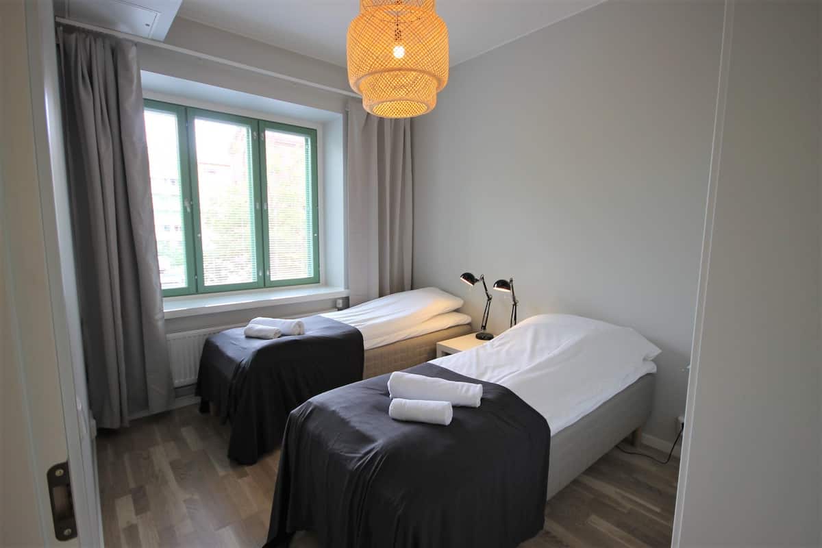Una habitación de hotel con dos camas, una ventana con cortinas, una lámpara colgante y un radiador.