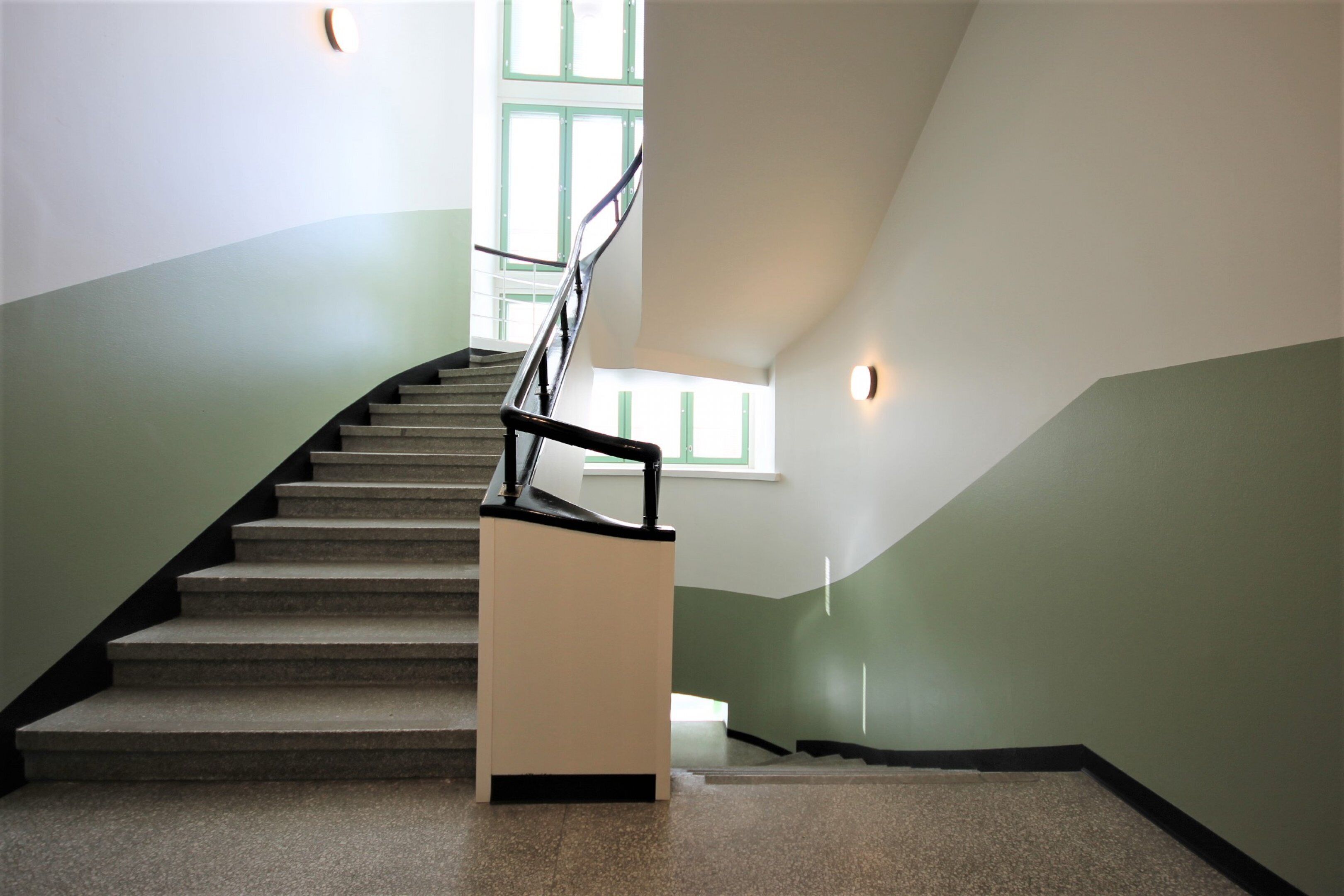 Eine Treppe mit Geländer, mit Teppich belegten Stufen und zweifarbig gestrichenen Wänden.
