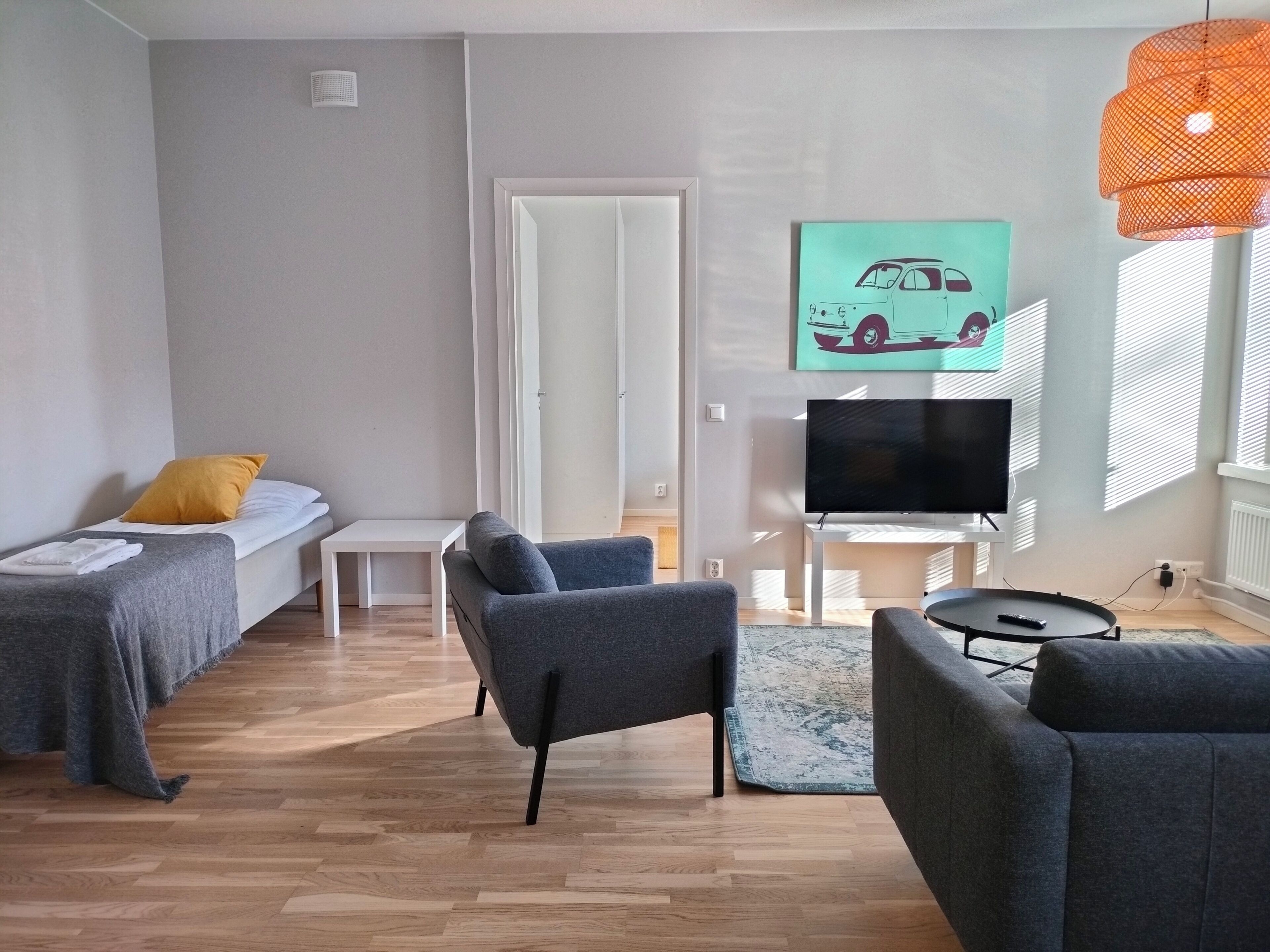 A modern living room with a sofa, a TV, and a painting of a car on the wall.