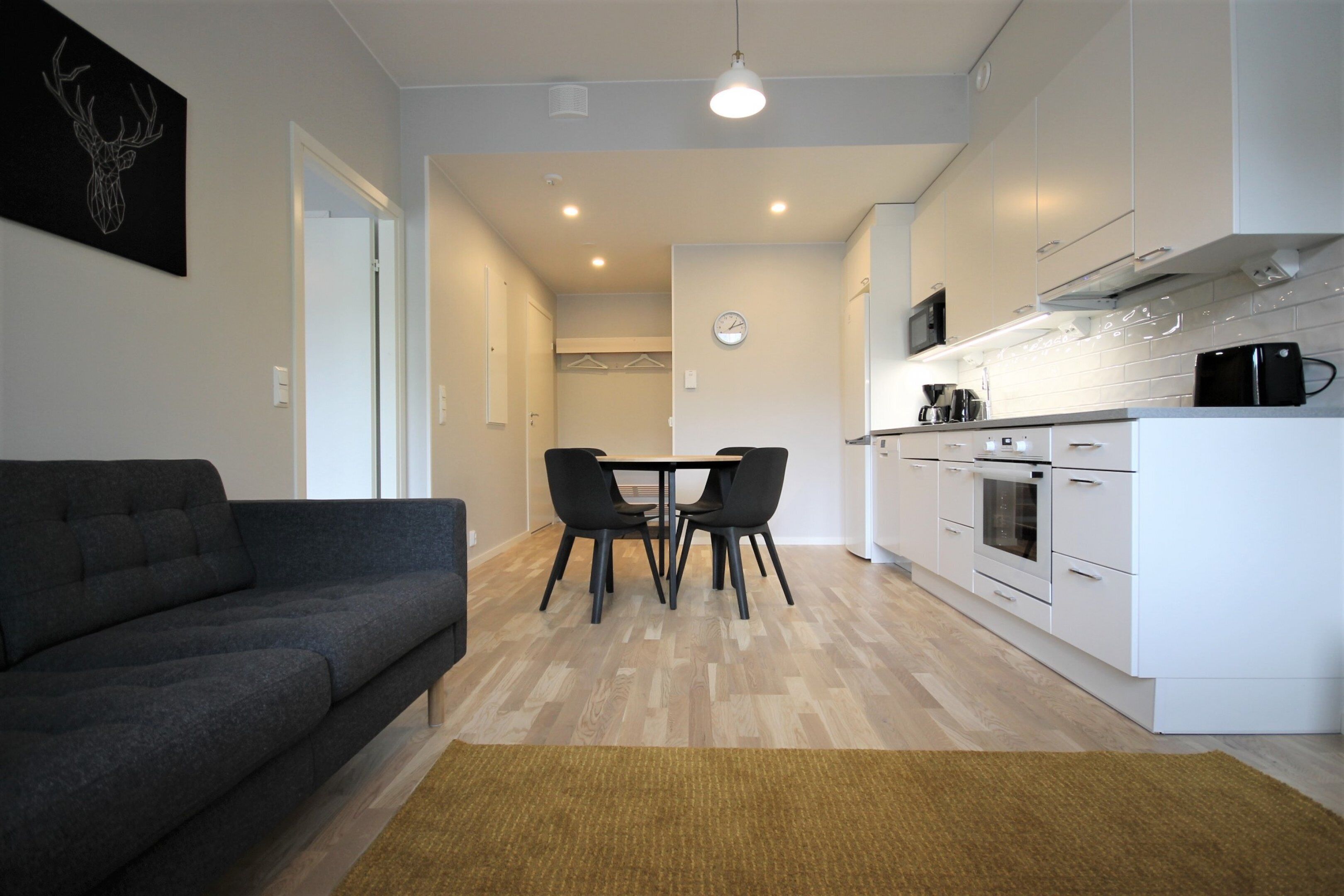 A modern living room with a sofa, a dining table with chairs, and a kitchen area with white cabinets and appliances.