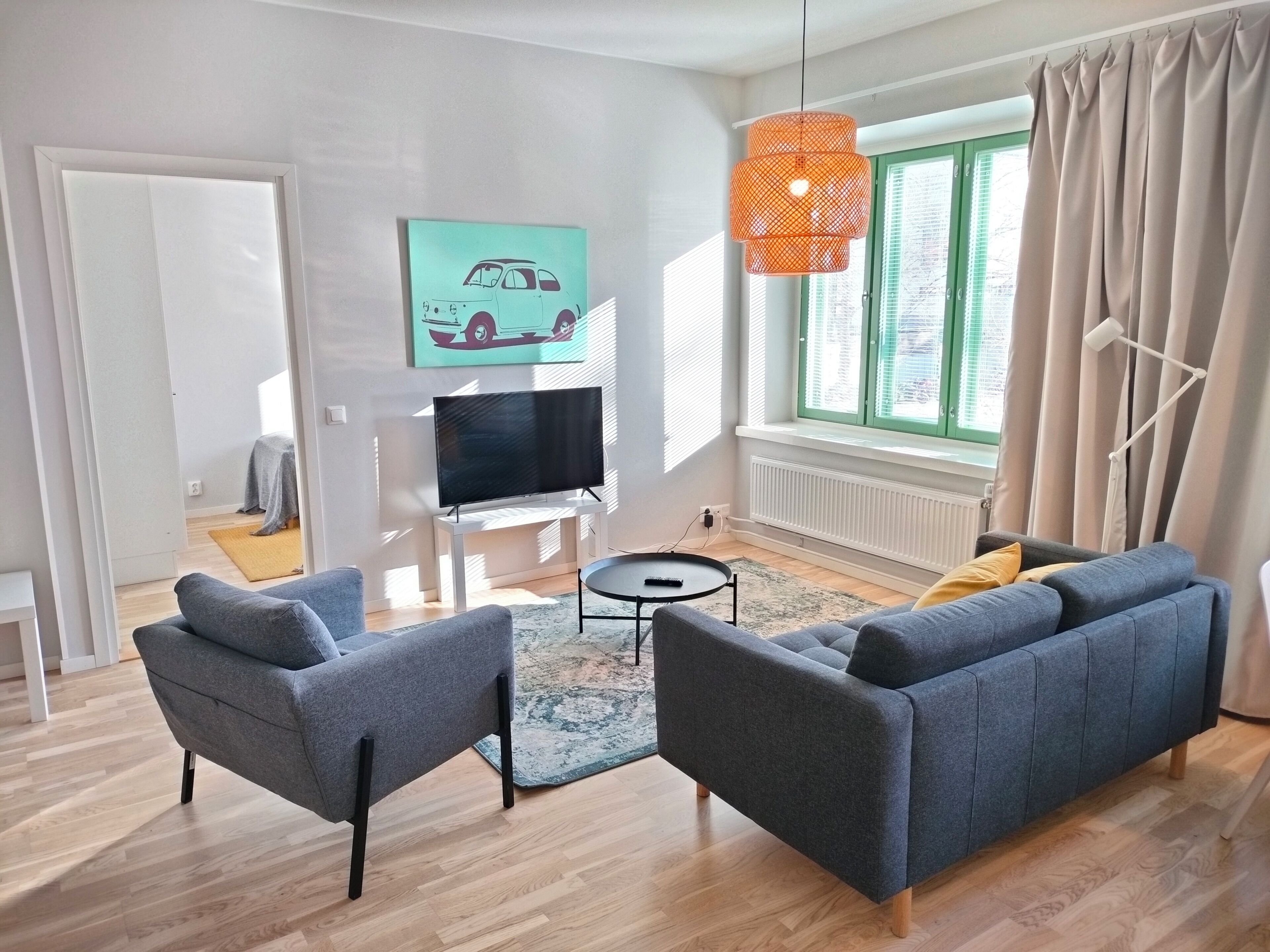 A modern living room with a sofa set, a TV, and a painting on the wall.