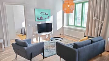 A modern living room with a sofa set, a TV, and a painting on the wall.