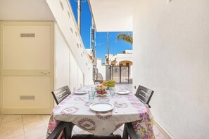 Uma área de refeições com uma mesa posta para dois, uma tigela de frutas e vista para a rua.