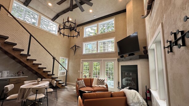 A spacious living area with a fireplace, a dining table, and a sofa. There are large windows and a ceiling fan. - Lux Cabin 2/2, HotTub, Wood Fireplace, Soaker Tub, Firepit, Walk to Lighthouse (Tremont)