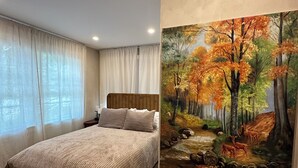A bedroom with a bed, a nightstand, a painting of a forest scene, and a window with curtains. - Lux Cabin 2/2, HotTub, Wood Fireplace, Soaker Tub, Firepit, Walk to Lighthouse (Tremont)