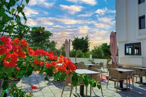 Una terrazza esterna con tavoli e sedie, immersa nel verde e adiacente a un edificio.