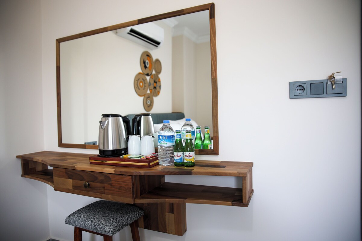 A wooden desk with a mirror, a kettle, a coffee maker, and bottled water.