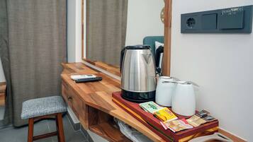 A compact kitchenette with a coffee maker, kettle, and tea pot on a wooden countertop.