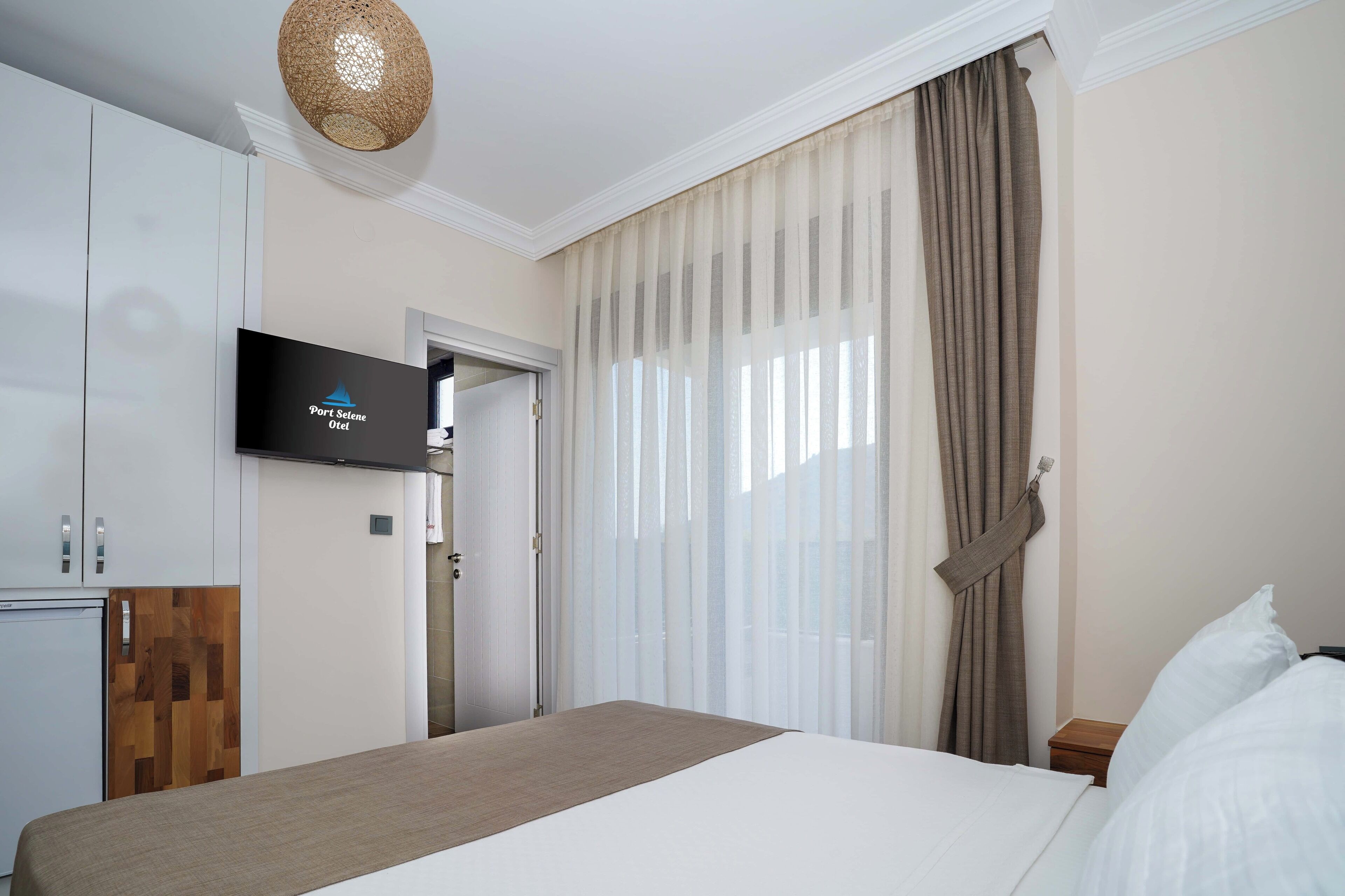 A hotel room with a bed, a television mounted on the wall, a wardrobe, and a door leading to another room.