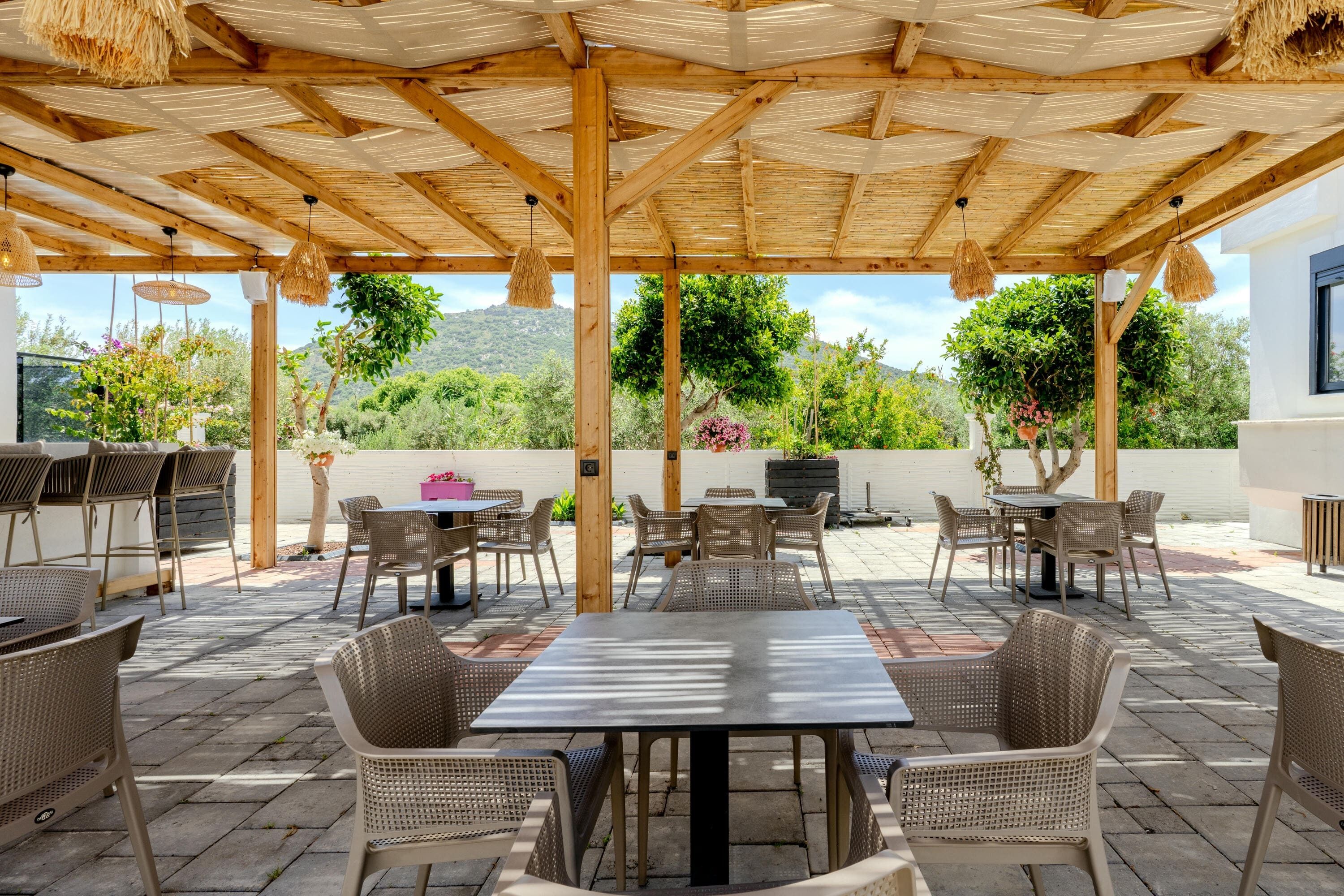 Une terrasse extérieure dotée d’une pergola en bois, de meubles en osier et offrant une vue sur la verdure et les collines.
