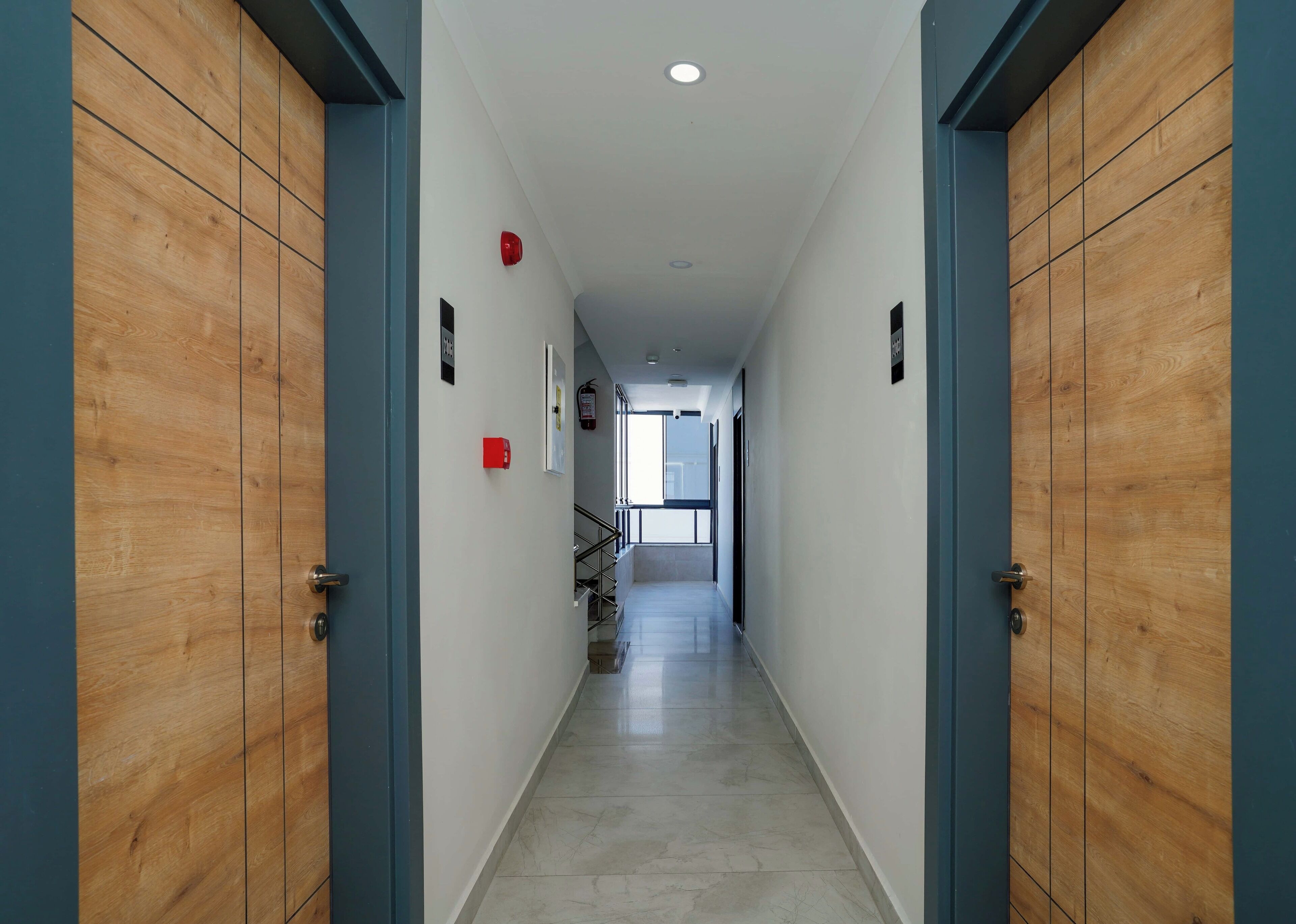 Un pasillo con puertas de madera y suelo de baldosas, que conduce a una escalera.