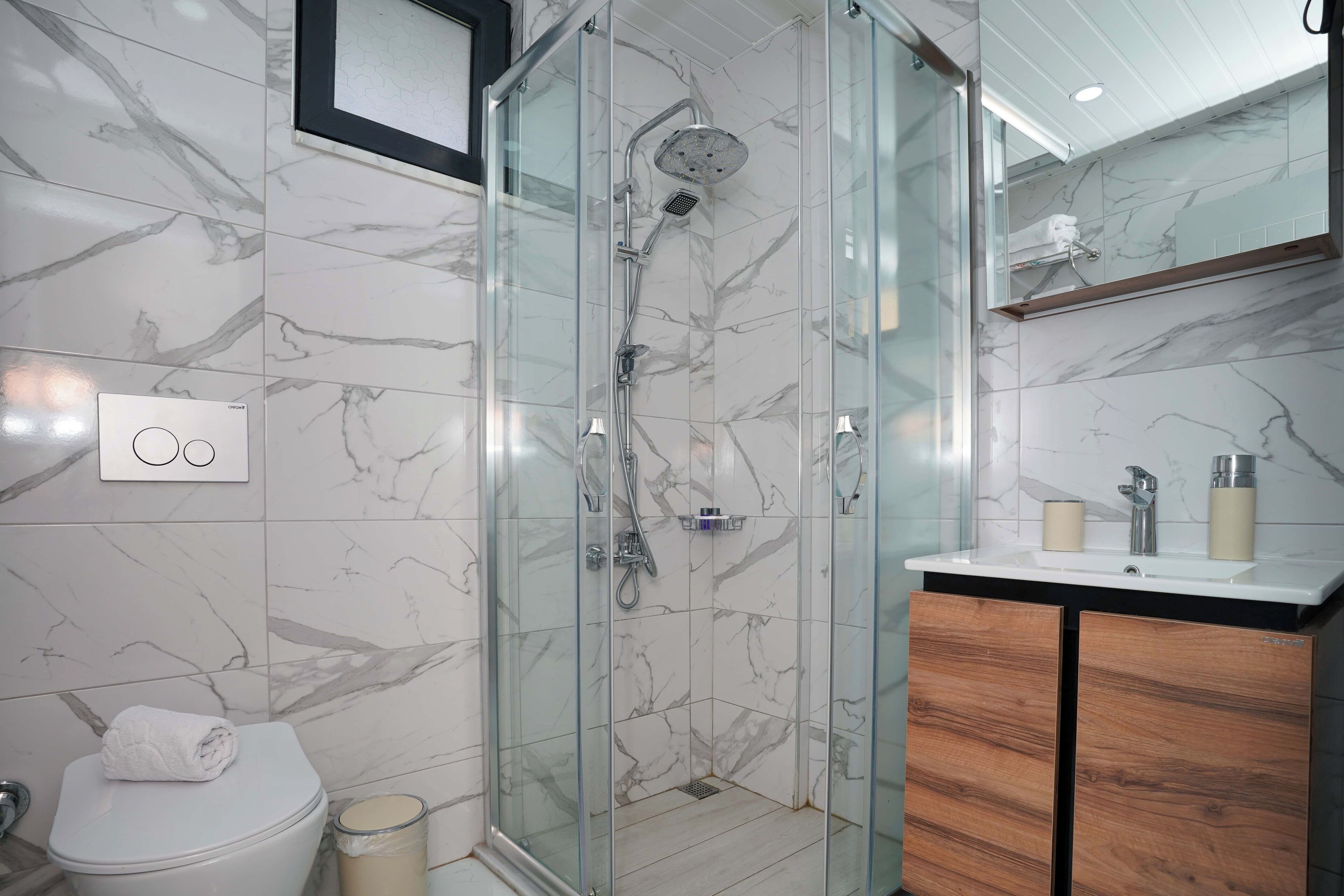 A modern bathroom with a glass-enclosed shower, a white toilet, and a wooden vanity with a sink.