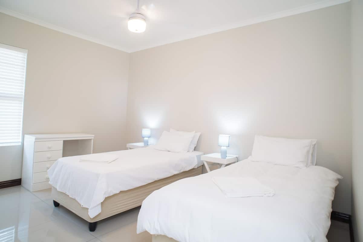 A clean, minimalist hotel room with two beds, bedside tables, and a white dresser.
