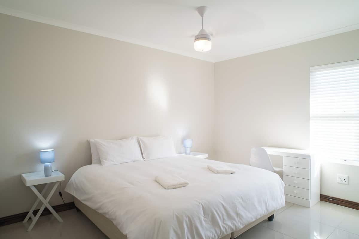 A minimalist bedroom with a bed, bedside tables, a desk, and a ceiling fan.