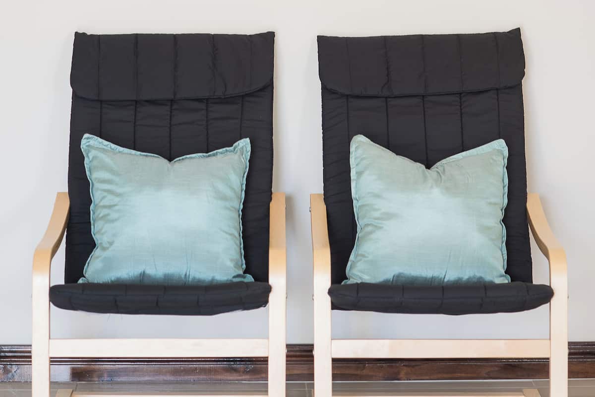 Two armchairs with black upholstery and teal cushions, positioned in front of a wall with a framed abstract artwork.