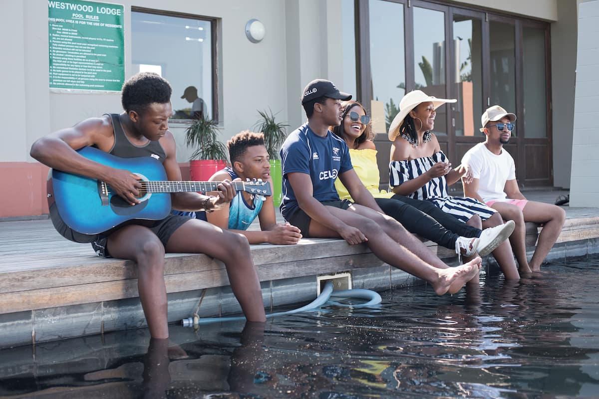 A group of people sitting by a pool with a sign indicating pool rules.
