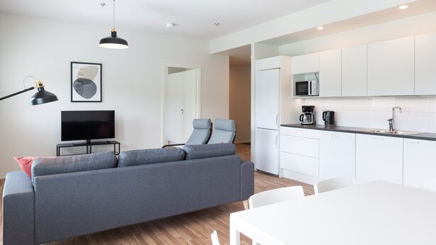A modern living room with a grey sofa, a TV, and a dining area with a white table. - Forenom Serviced Apts Turku Pansio (Turku)