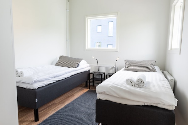 A room with two beds, a small table, and a window with a view of a building. - Forenom Serviced Apts Turku Pansio (Turku)