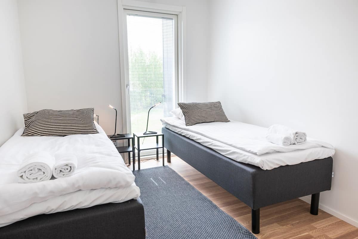 A modern hotel room with two single beds, a small desk, and a chair.