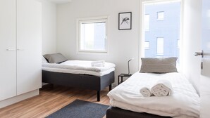 Ett modernt sovrum med två sängar, en garderob, ett fönster och en inramad tavla på väggen.