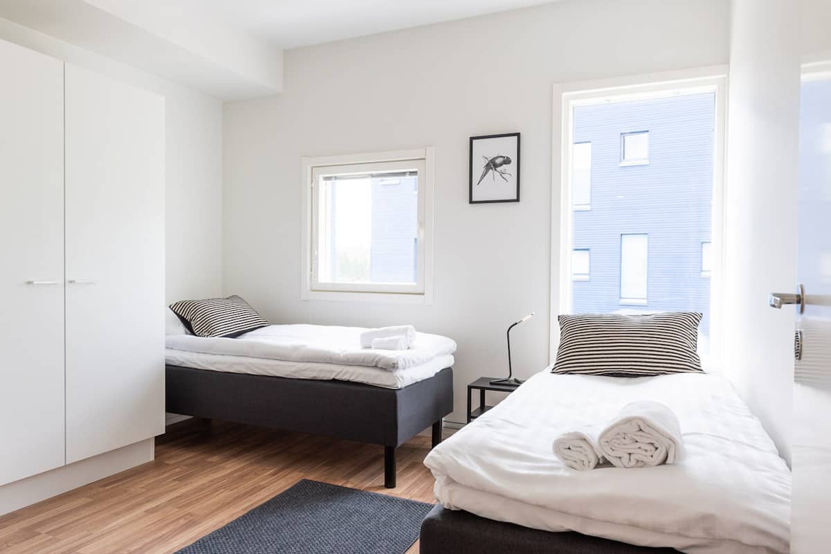 A modern bedroom with two beds, a wardrobe, a window, and a framed picture on the wall.