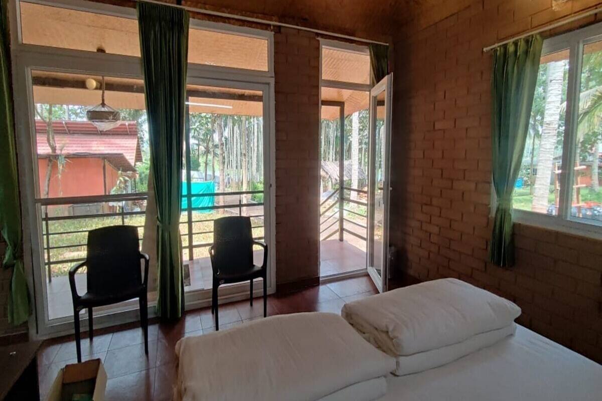 A room with a bed, two chairs, and a view of a pool and greenery outside.