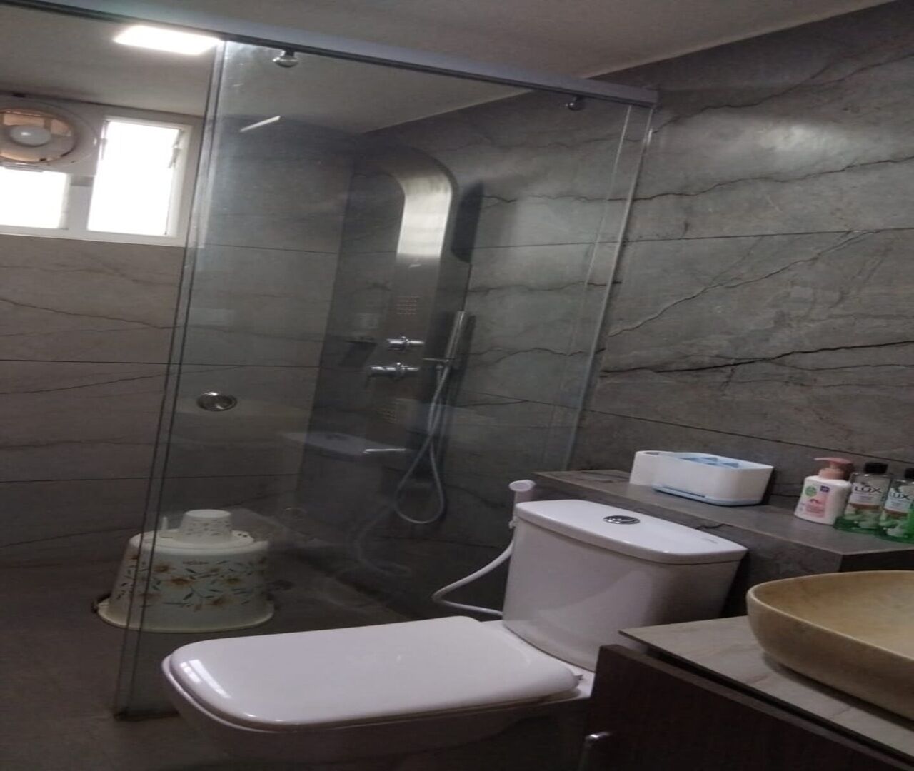 A bathroom with a glass-enclosed shower, a toilet, and a sink area with toiletries.