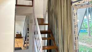 A modern interior with a wooden staircase, a view through a window with curtains, and a small table with bottles. - Cosmic Connect Trails Kabini (Heggadadevankote)