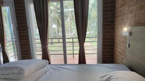 A bedroom with a large bed, a brick wall, and a view of palm trees through a sliding glass door. - Cosmic Connect Trails Kabini (Heggadadevankote)