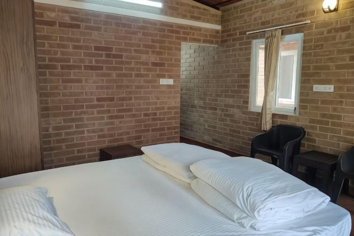 A room with a brick wall, a bed with white bedding, a chair, and a window with curtains.