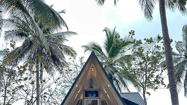 A modern, triangular-shaped building with a balcony, surrounded by palm trees. - Cosmic Connect Trails Kabini (Heggadadevankote)