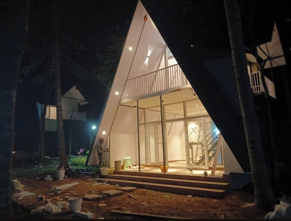A triangular tent-like structure with a glass facade, a staircase leading to the entrance, and construction materials scattered around.
