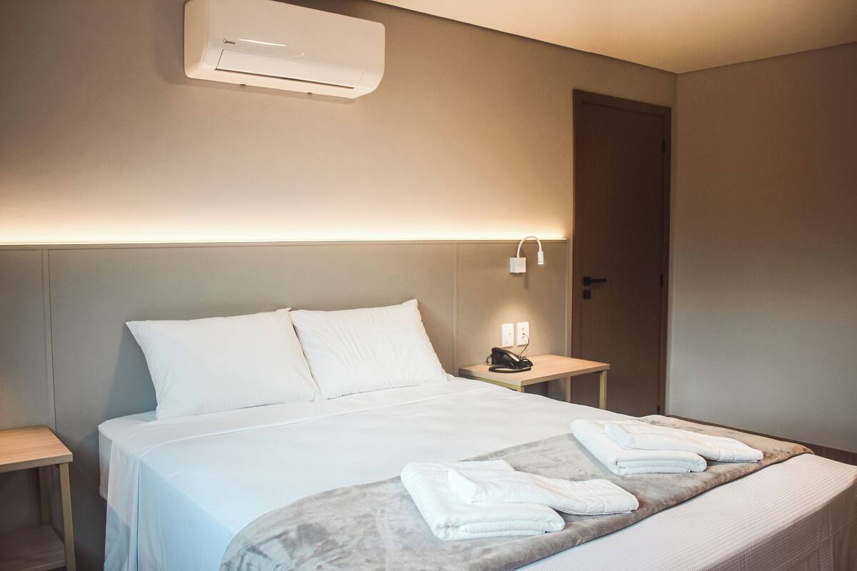 Habitación de hotel con cama, mesita de noche y aire acondicionado de pared.