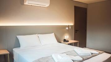 A hotel room with a bed, bedside table, and a wall-mounted air conditioner.